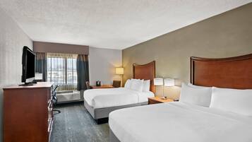 A hotel room with two beds, a desk with a flat-screen TV, a dresser, and a window with curtains.