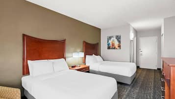 A hotel room with two beds, a nightstand with a lamp, a painting on the wall, and a wooden dresser.