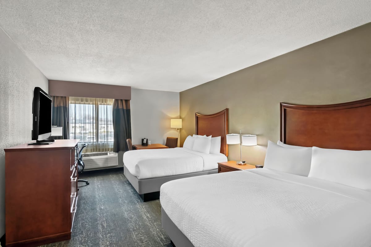 Une chambre d’hôtel avec deux lits, un bureau avec une télévision et une vue sur la ville grâce à de grandes fenêtres.