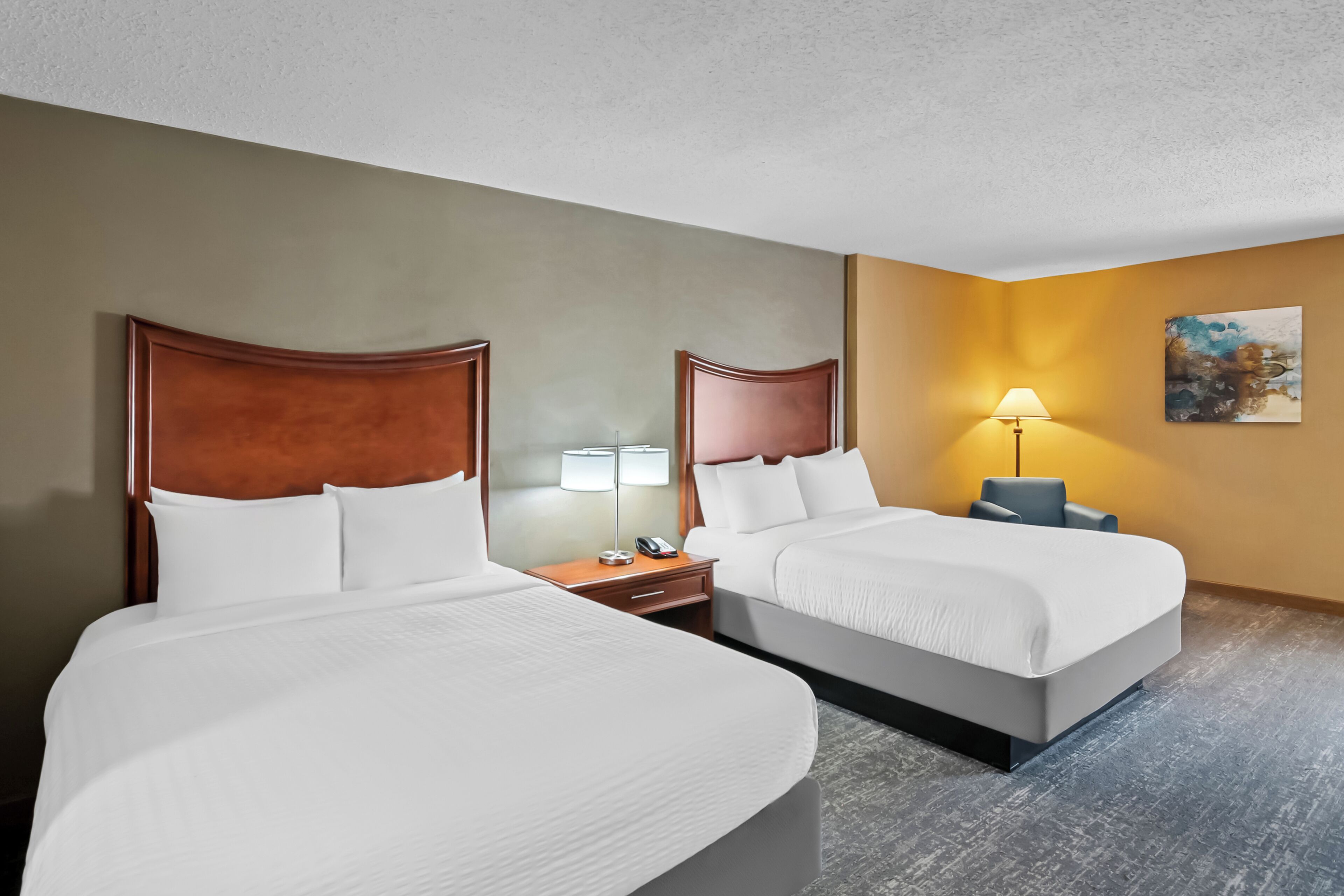 A hotel room with two beds, a nightstand, a lamp, and a painting on the wall.