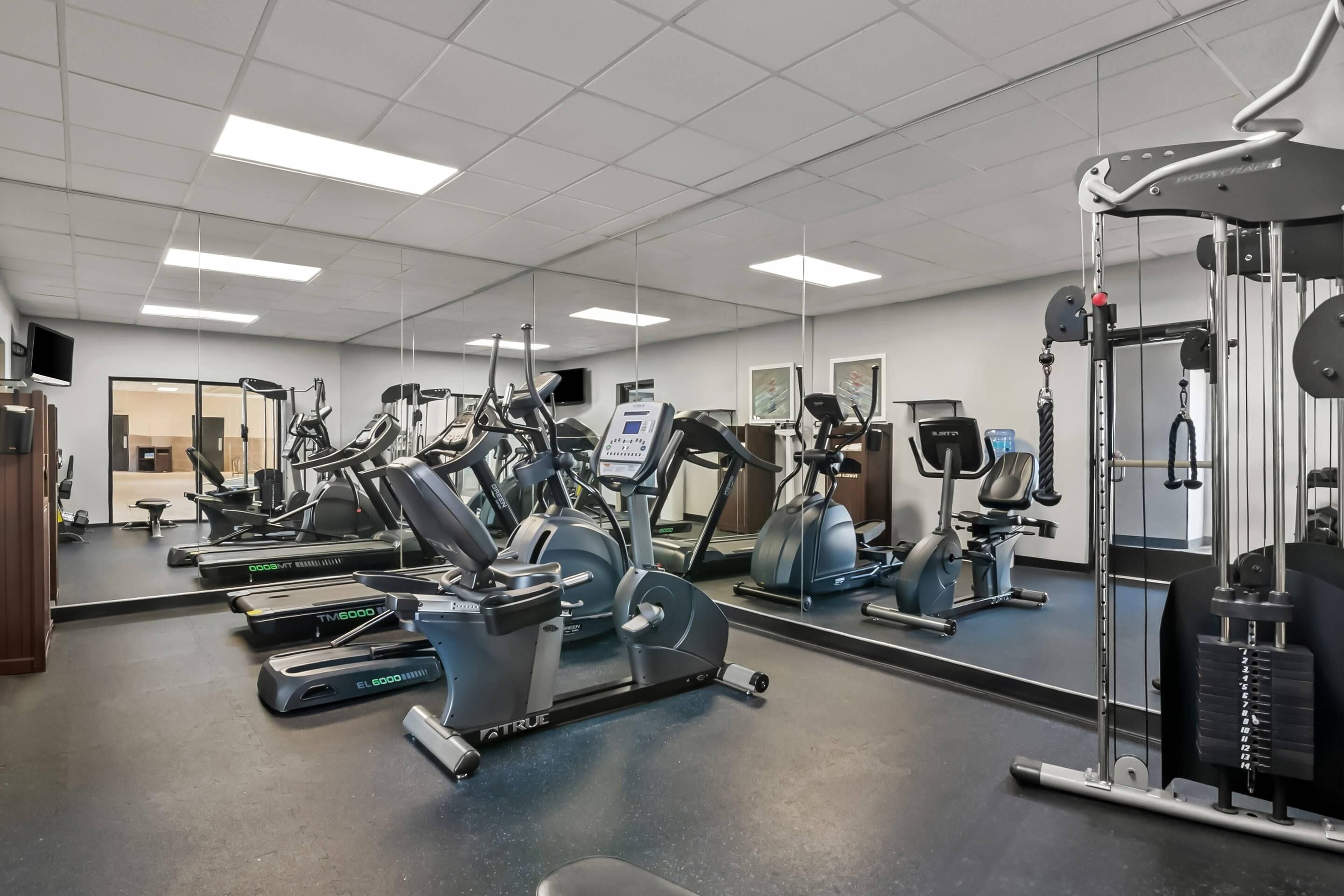 A gym with various exercise machines, a mirrored wall, and a television.