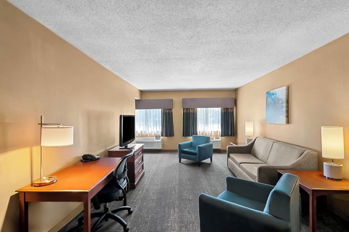 Une chambre d’hôtel équipée d’un bureau, de deux fauteuils, d’un canapé, d’une télévision et d’un tableau au mur.