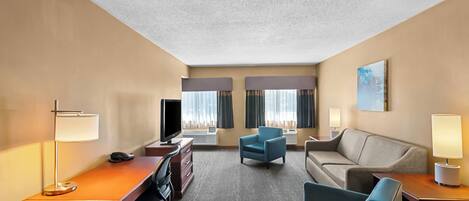 A hotel room with a desk, two armchairs, a sofa, a TV, and a painting on the wall.