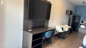 A modern kitchenette with a flat-screen TV, a refrigerator, and a dining area with a table and chairs. - Studio 6 Corona, CA - West (Corona)