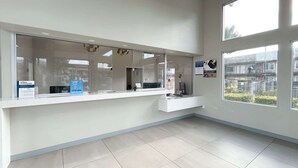 A modern reception area with a glass partition, a counter, and a view of the outside. - Studio 6 Corona, CA - West (Corona)