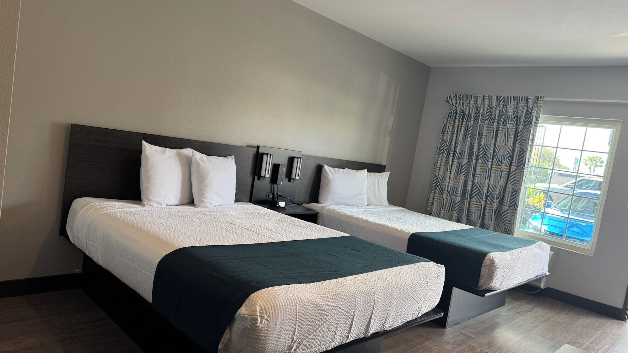 Une chambre d’hôtel avec deux lits, une grande fenêtre avec des rideaux à motifs et une vue sur un parking.