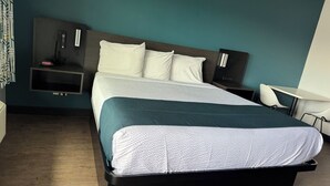 A hotel room with a large bed, a bedside table, a chair, and a desk. - Studio 6 Corona, CA - West (Corona)