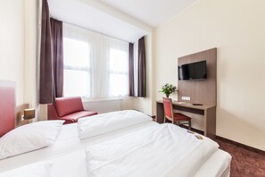 A hotel room with a bed, a desk, a chair, a TV, and a window with curtains. - Hotel Maxim Düsseldorf City (Düsseldorf)