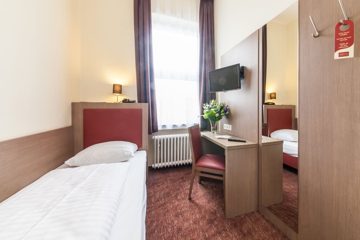 Una habitación de hotel con una cama, un escritorio con silla, un televisor y un espejo.