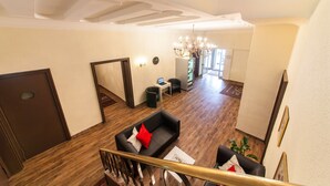 Un hall d’entrée spacieux avec un plancher en bois, un canapé noir agrémenté de coussins rouges et blancs, un lustre et un escalier.