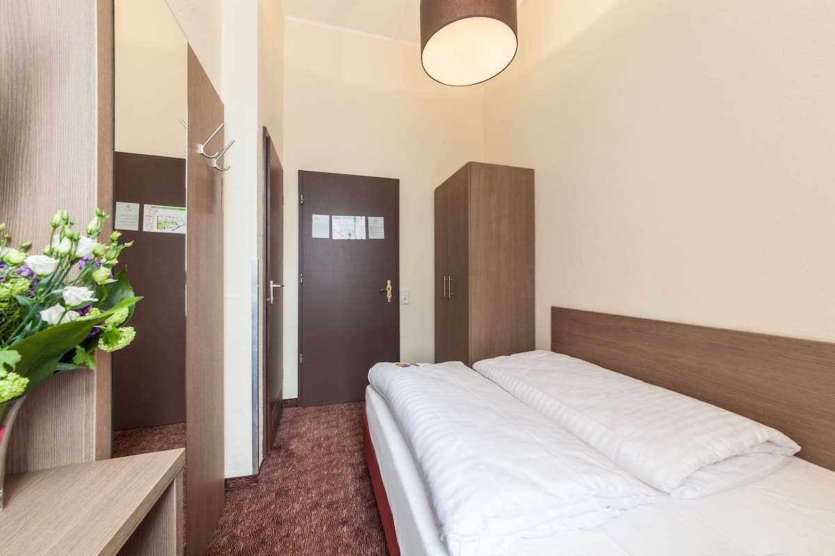 Habitación de hotel con cama, armario de madera, escritorio con un florero y puerta con avisos.