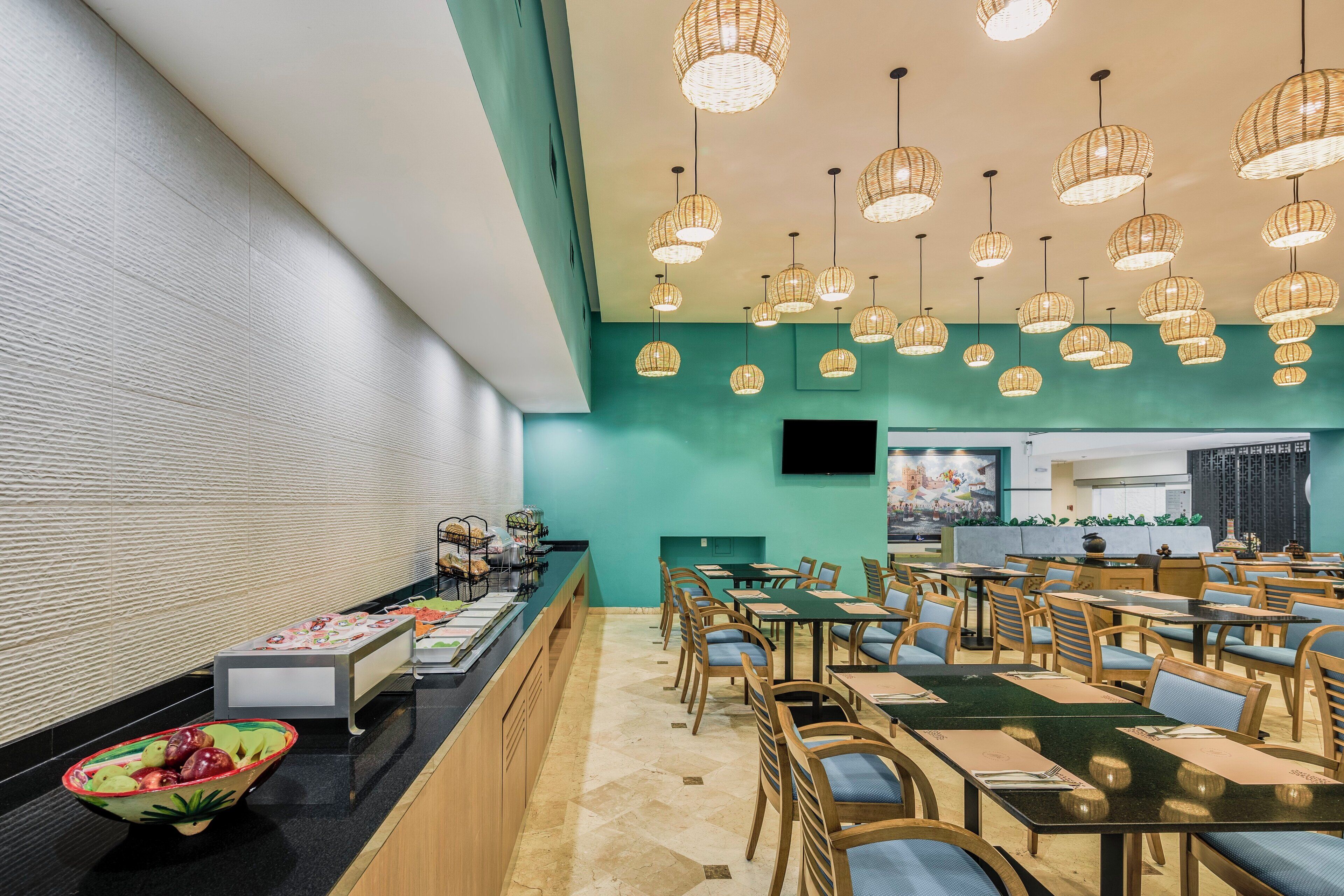 A restaurant with multiple tables and chairs, a buffet area, and hanging wicker light fixtures.