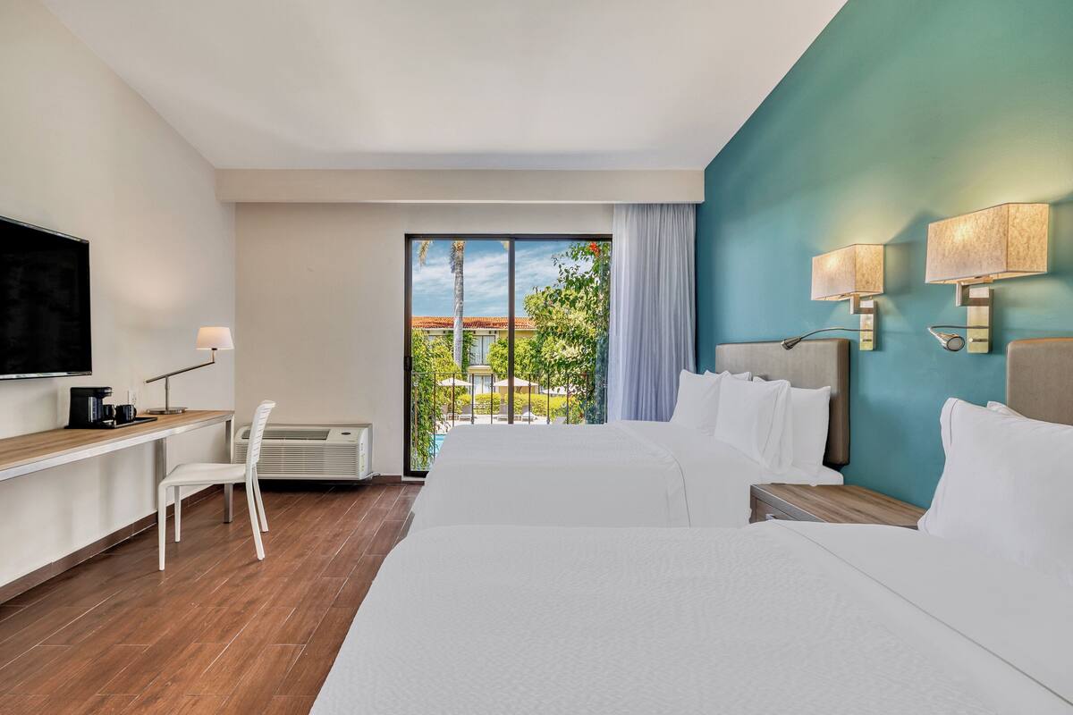 Ein Hotelzimmer mit einem großen Bett, einem Schreibtisch mit Stuhl, einem Fernseher und Blick ins Freie.