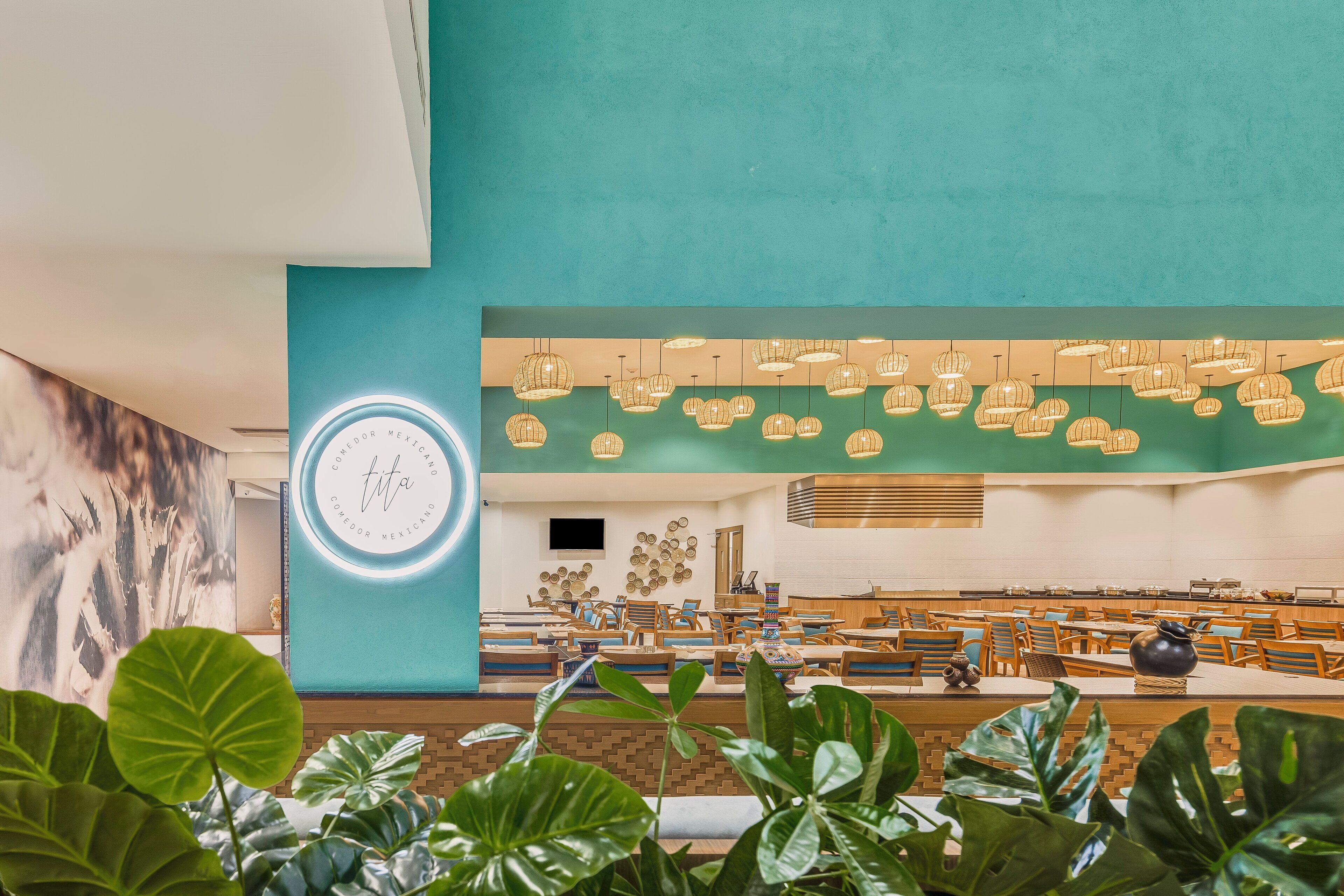 A spacious indoor area with a teal wall, hanging pendant lights, and a seating area with tables and chairs.