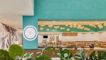 A spacious indoor area with a teal wall, hanging pendant lights, and a seating area with tables and chairs.