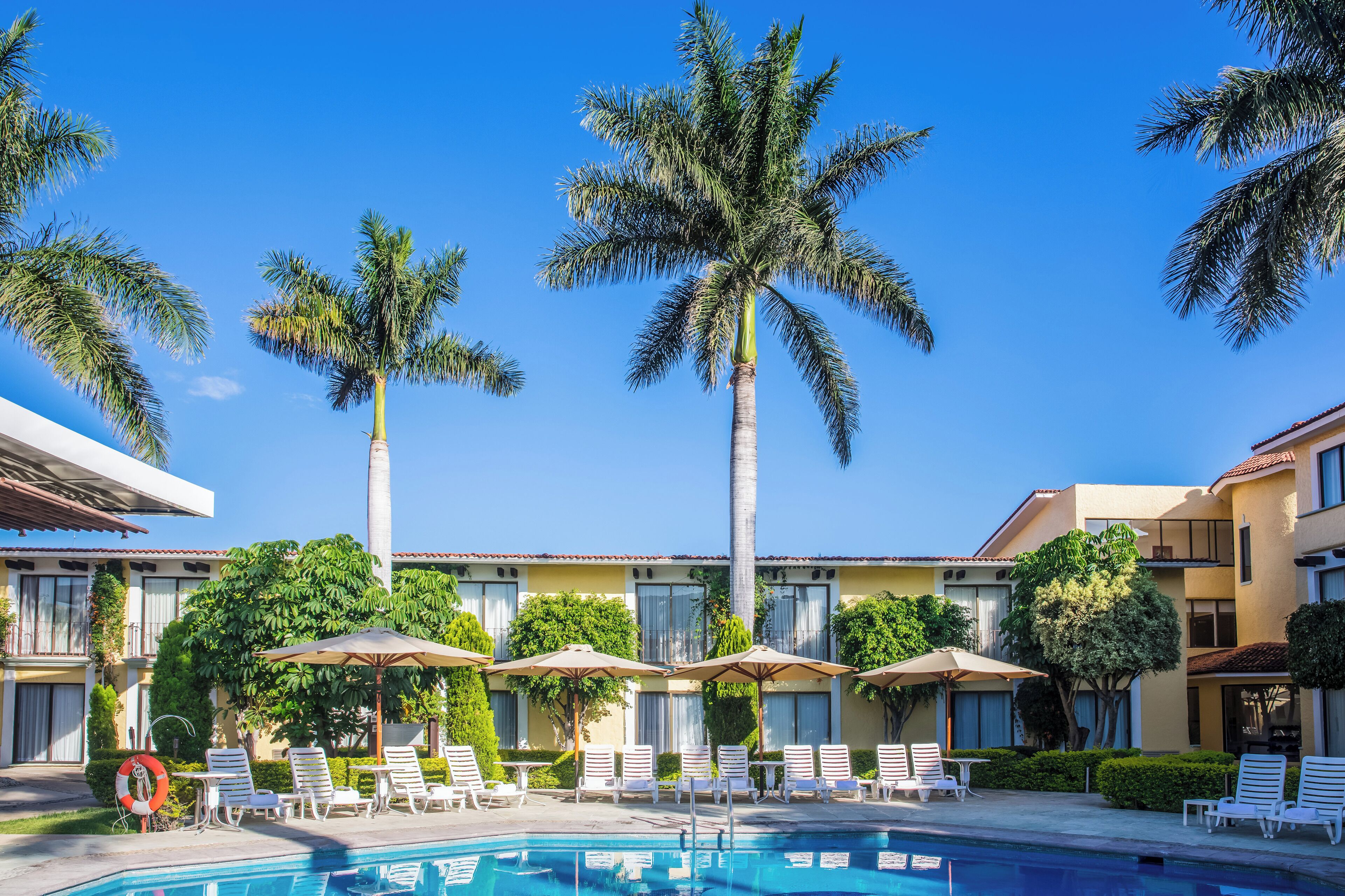 A hotel courtyard with a swimming pool, palm trees, lounge chairs, and umbrellas.