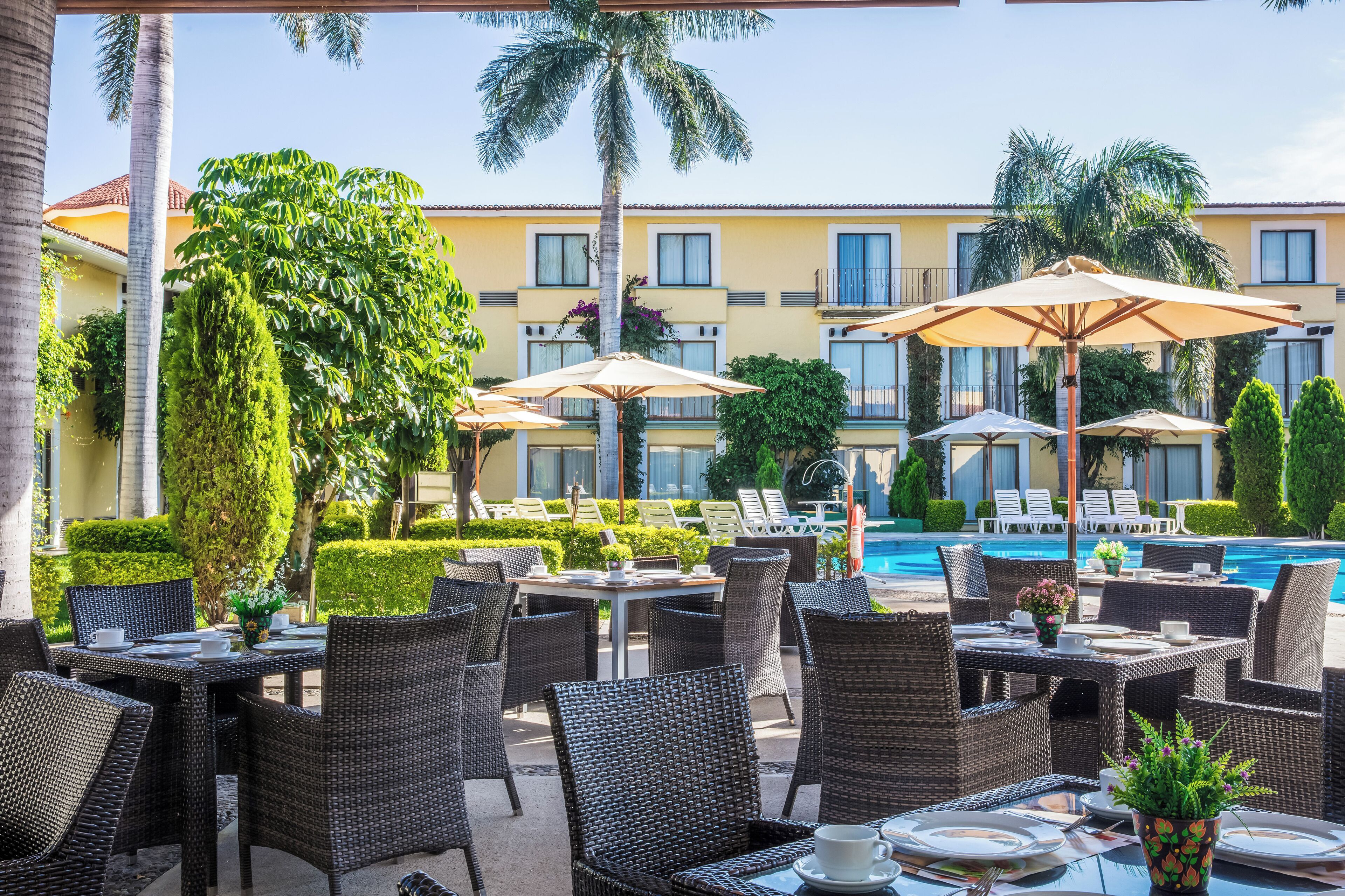 A poolside area with wicker furniture, umbrellas, and a pool in the background.