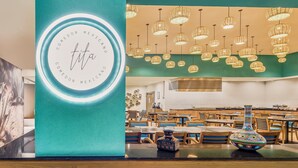A restaurant interior with teal walls, hanging wicker chandeliers, and a central decorative vase. - Fiesta Inn Oaxaca (Oaxaca)
