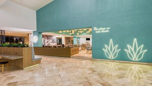 A modern lobby with a teal wall, a reception desk, and a seating area. - Fiesta Inn Oaxaca (Oaxaca)