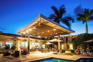 An outdoor pool area with lounge chairs and umbrellas, a covered seating area, and a bar.