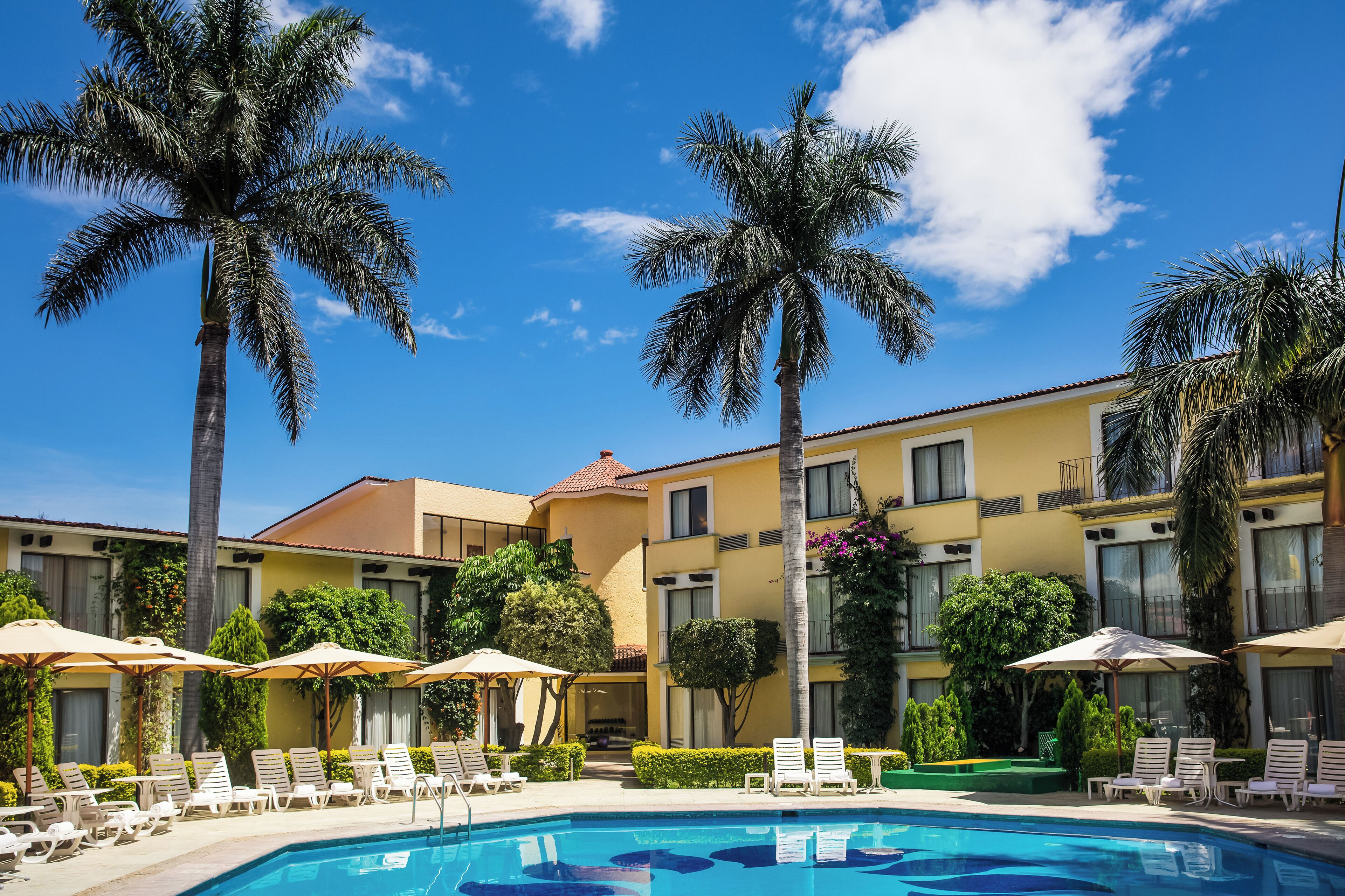 A hotel with a swimming pool, palm trees, and lounge chairs.
