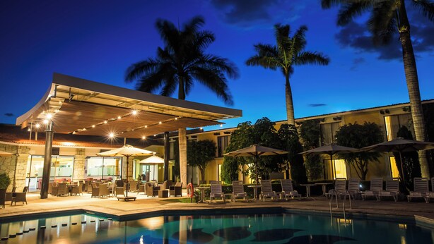 A poolside area with lounge chairs and umbrellas, a covered seating area, and a pool. - Fiesta Inn Oaxaca (Oaxaca)