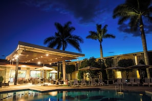 Zona de piscina con sillones de descanso y sombrillas, un espacio de estar techado y una piscina.
