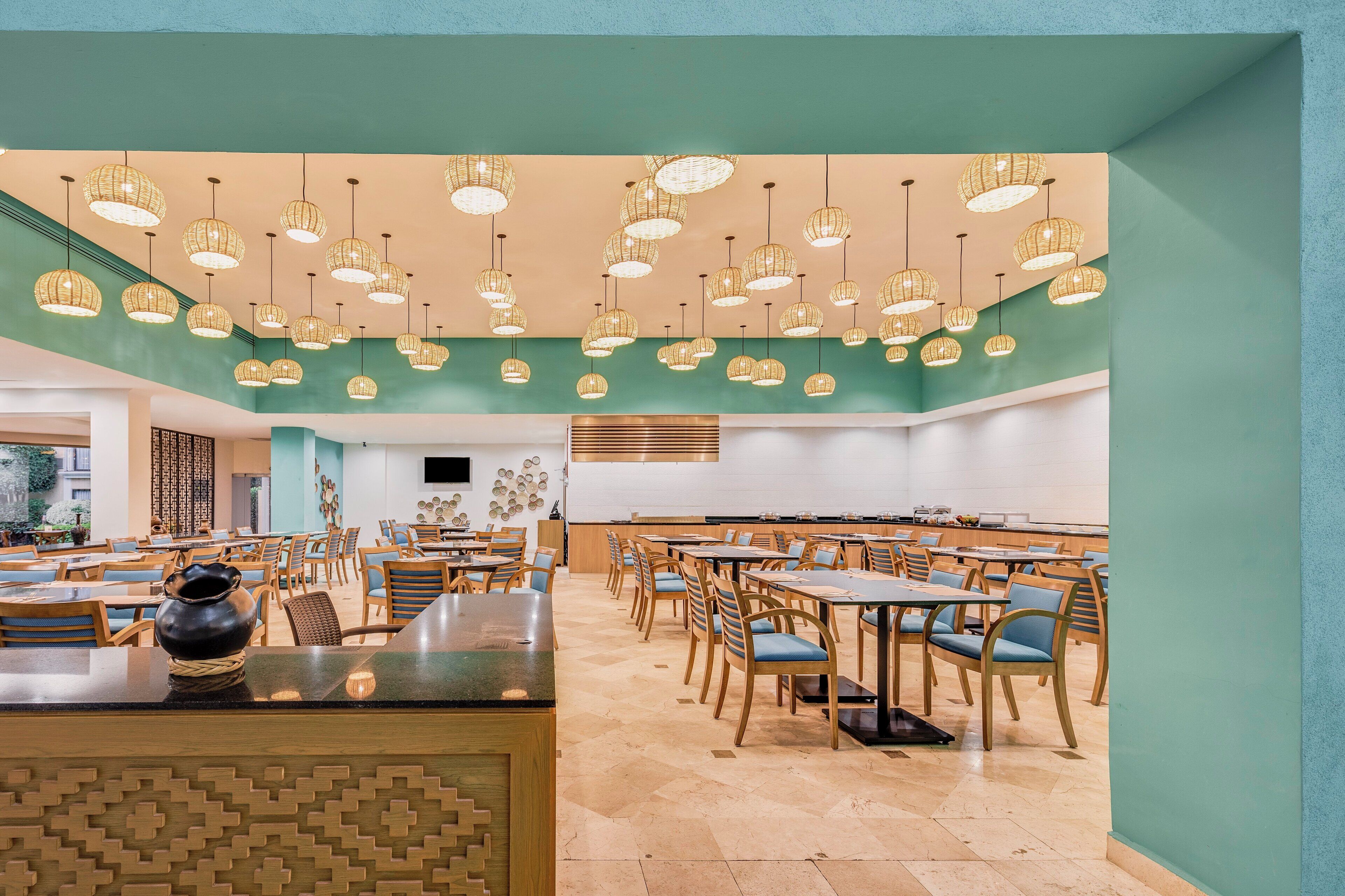 A spacious dining area with multiple tables and chairs, a central counter with a decorative item, and hanging wicker light fixtures.