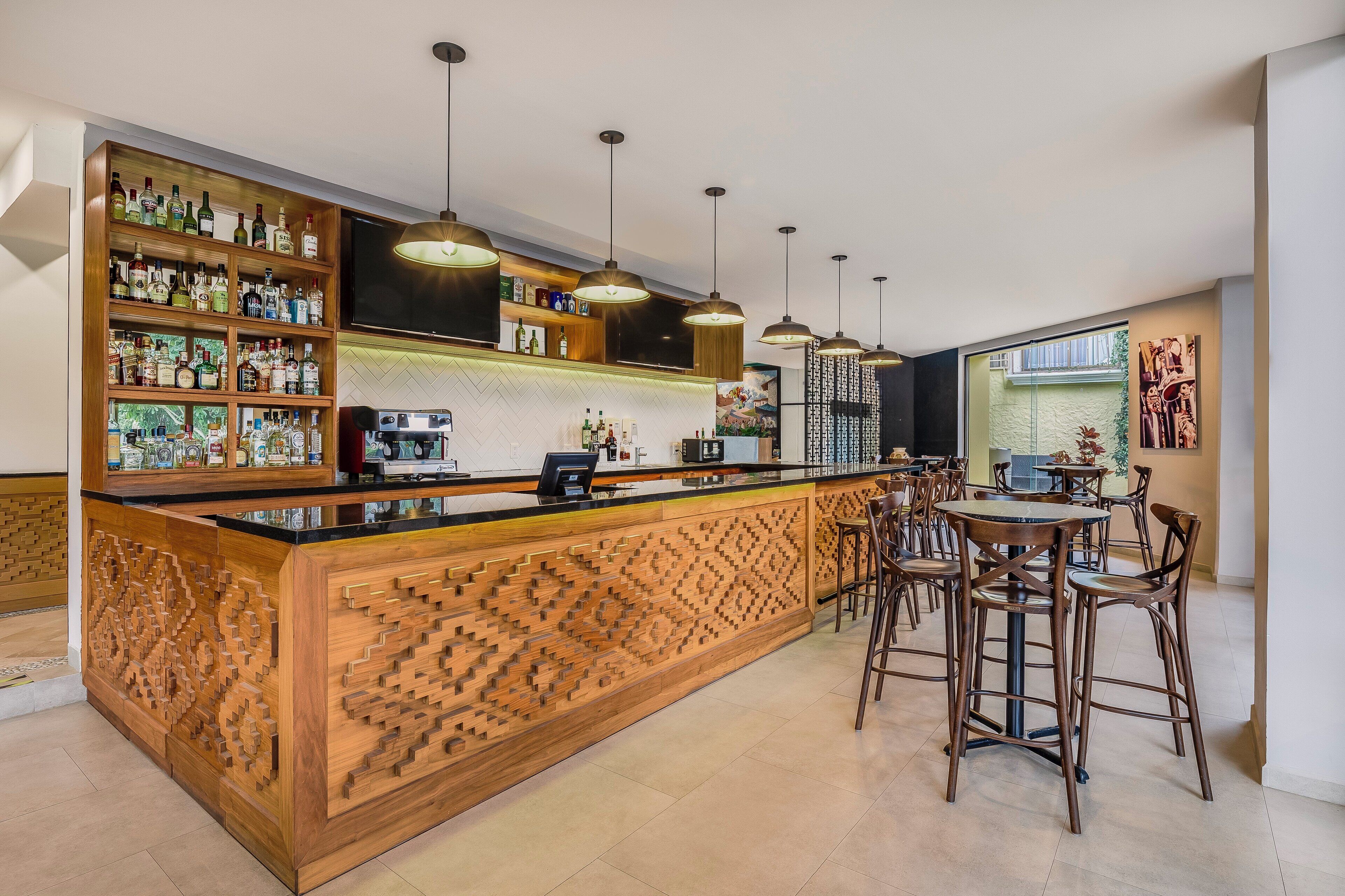 A bar area with a wooden counter, shelves with bottles, hanging lights, and bar stools.