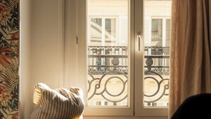 Una habitació amb finestra, un coixí sobre un tamboret i una persona amb roba negra.