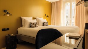 Habitació d'hotel amb un llit, dues làmpades penjades a la paret, un escriptori amb una cadira i una finestra amb cortines.