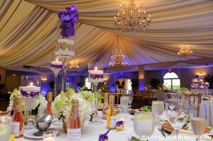 Un salón de banquetes con mesas escalonadas, candelabros y centros de mesa con flores.