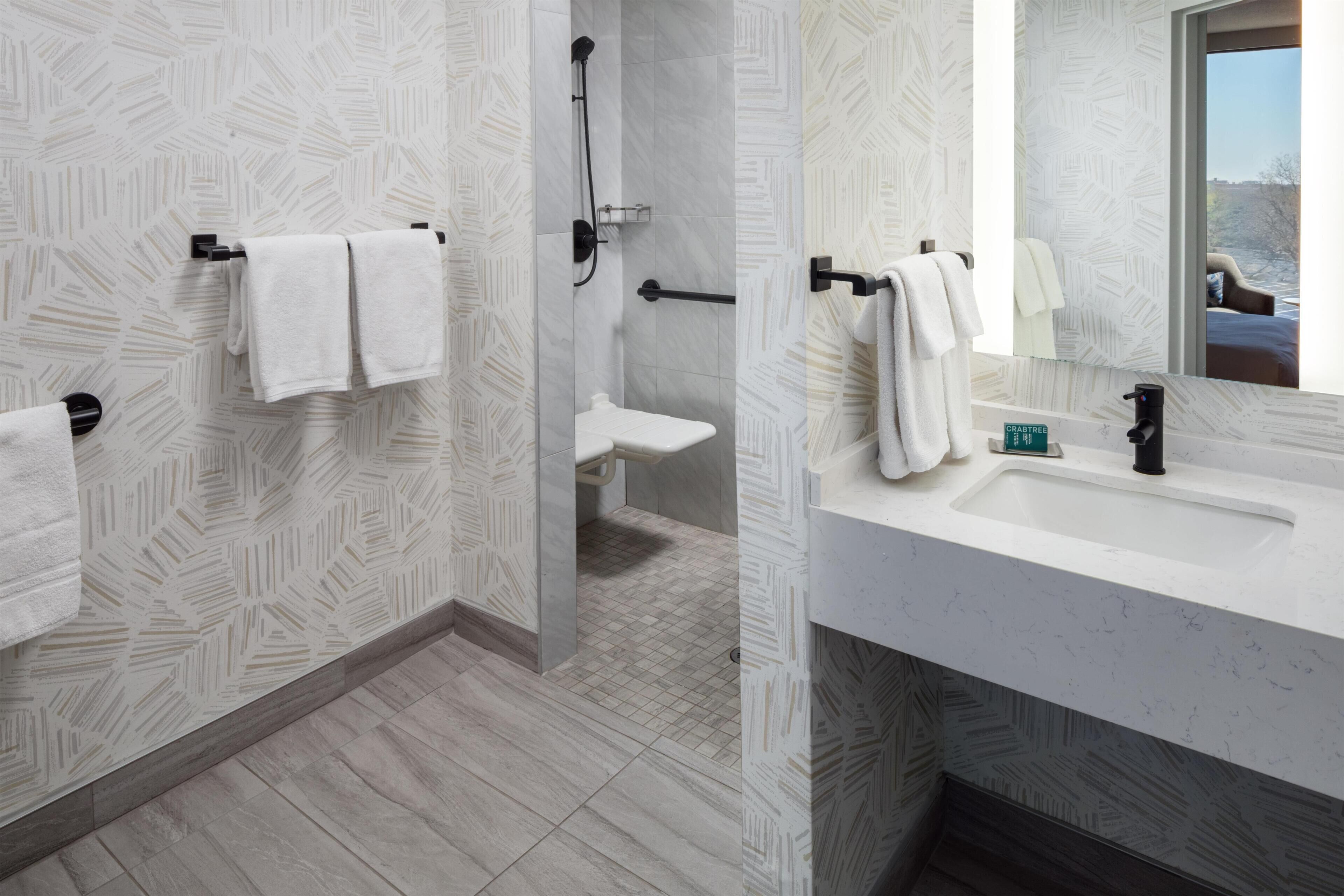 Un baño moderno con papel tapiz estampado, una ducha, un inodoro, un lavabo con espejo y vistas al exterior.
