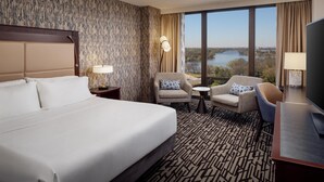 Habitación de hotel con una cama grande, dos sillones, un televisor y vistas a un lago.