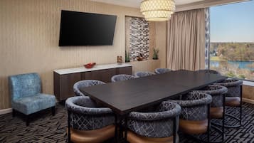 A conference room with a large table, chairs, a TV, and a view of a lake.