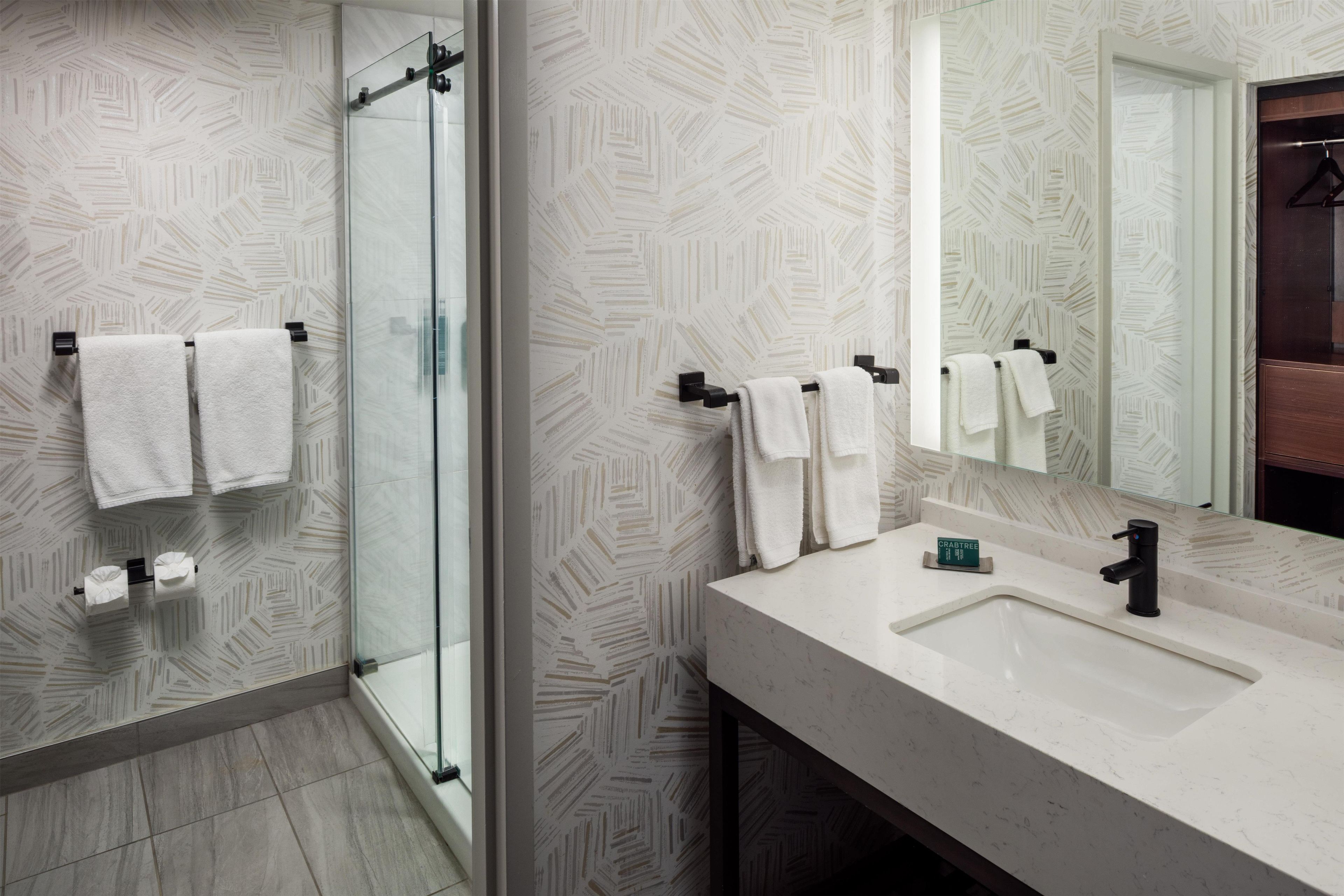 Un baño moderno con ducha de vidrio, lavamanos blanco y espejo.