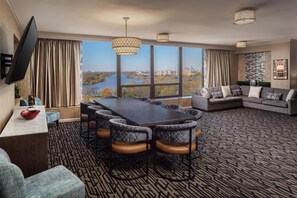 A modern hotel room with a large dining table, comfortable seating, a sofa, and a TV.
