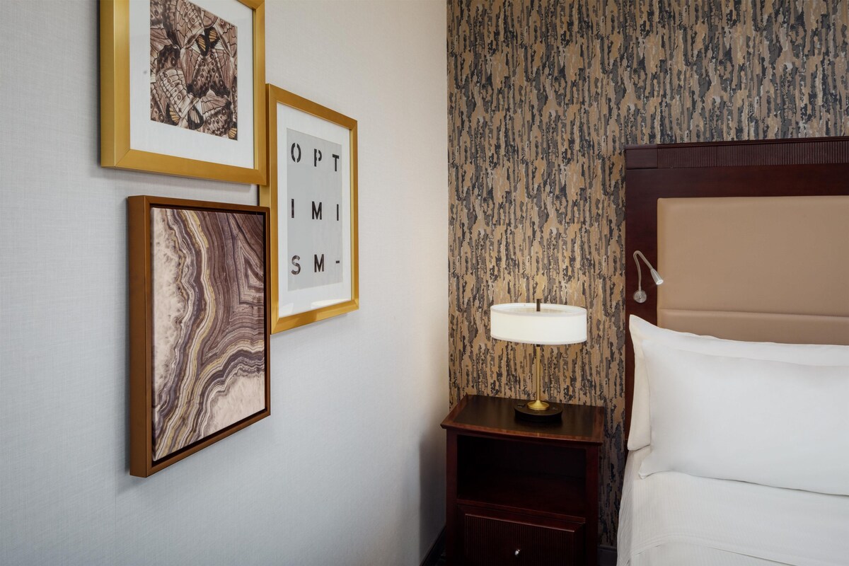 Una habitación de hotel con una cama, una mesita de noche con lámpara y tres cuadros en la pared.