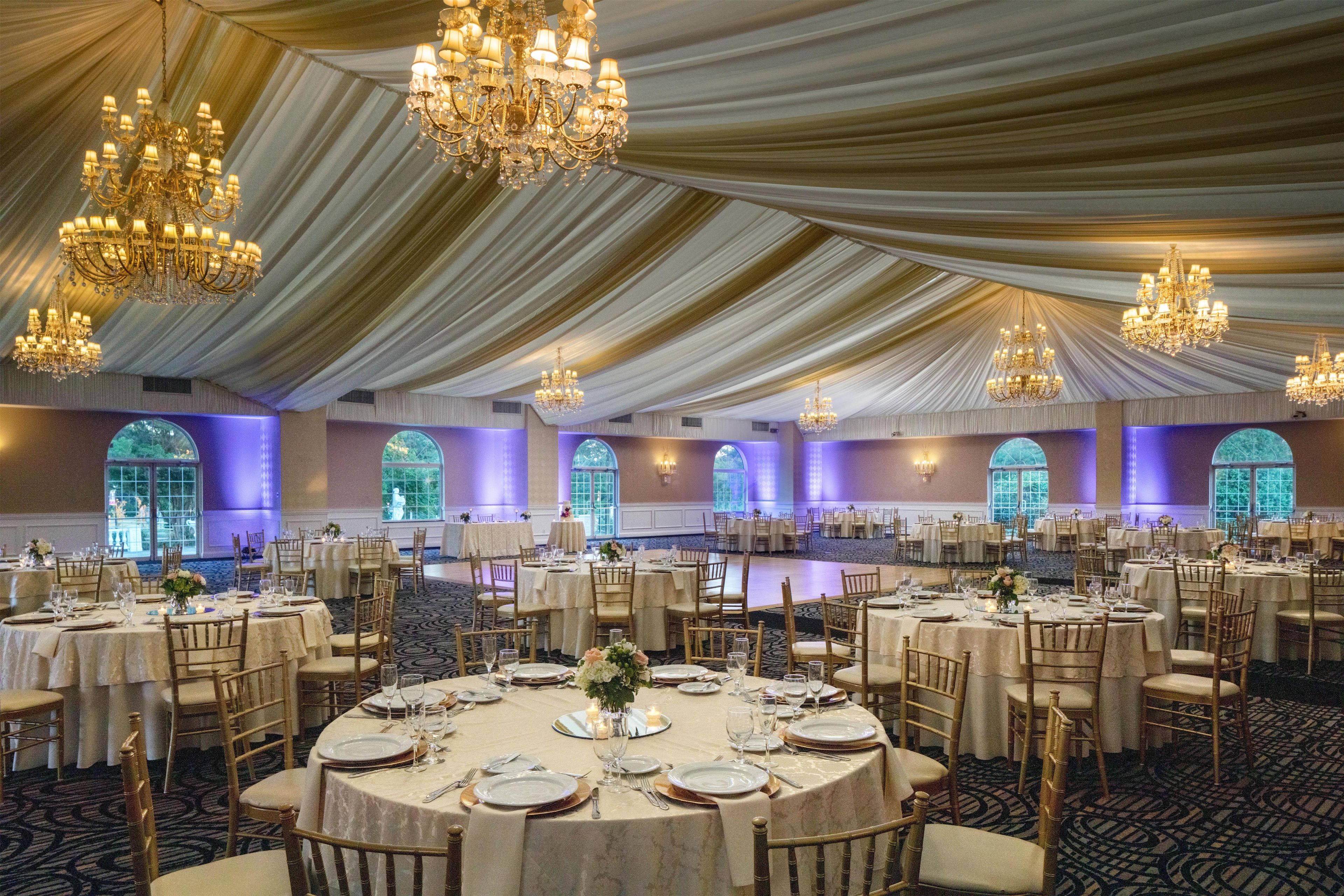 Un salón de banquetes con mesas redondas, candelabros y un techo alto cubierto con tela.