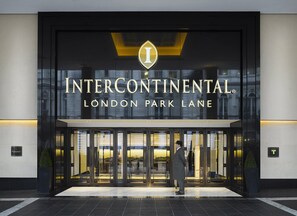 La entrada del hotel Intercontinental London Park Lane, con fachada de vidrio, y un hombre de pie frente a él.
