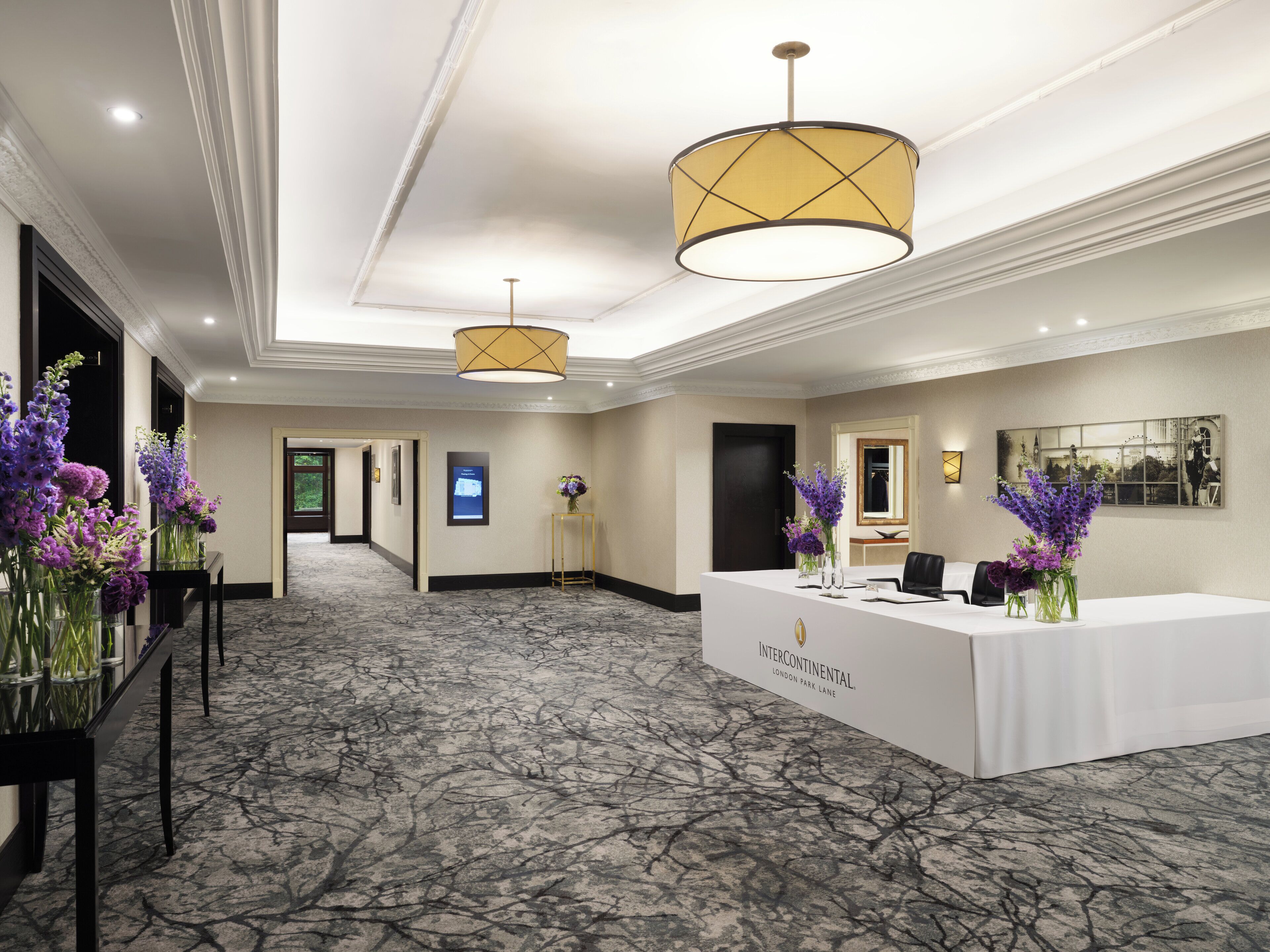 A hotel lobby with a reception desk, two chandeliers, and floral arrangements.