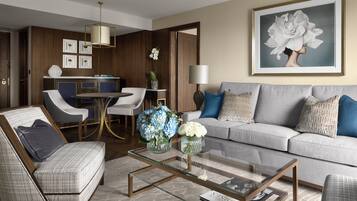 A modern living room with a grey sofa, two armchairs, a glass coffee table, and a dining area with a table and chairs.