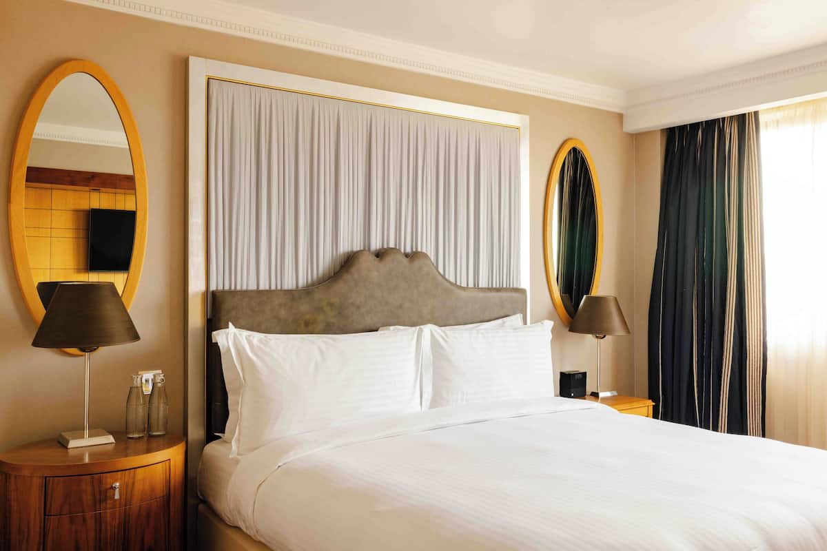 A neatly made bed with white linens, a wooden headboard, and two bedside tables with lamps and glass bottles.