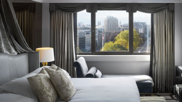 Une chambre d’hôtel avec un grand lit, un bureau et une vue sur le paysage urbain, visible à travers une fenêtre avec des rideaux.