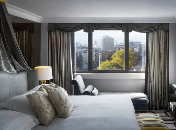 Habitación de hotel con una cama grande, un escritorio y vista a un paisaje urbano a través de una ventana con cortinas.