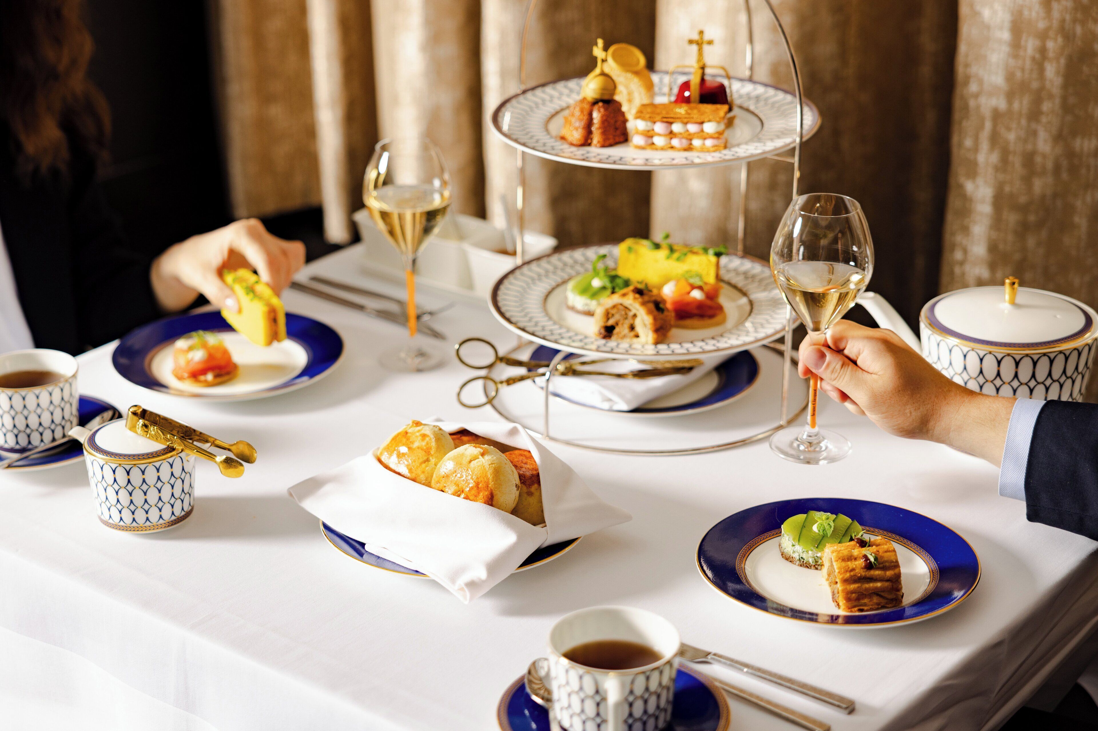 A table set with a variety of dishes, including a tiered dessert stand, a cup of coffee, and a glass of white wine.