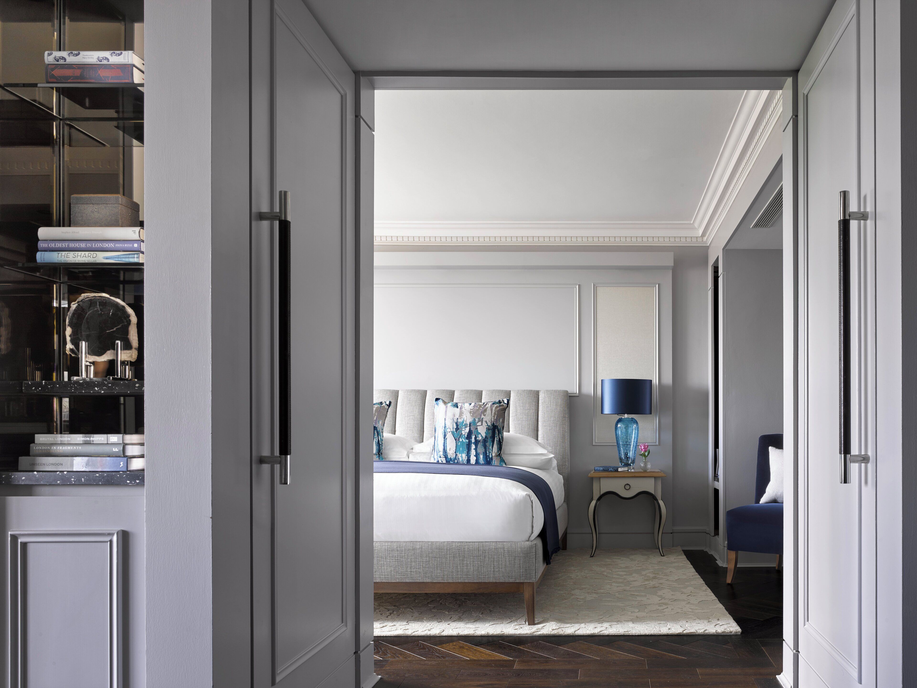 Une chambre à coucher comprenant un lit, une table de chevet, une lampe, une chaise et une bibliothèque avec des livres et des objets décoratifs.