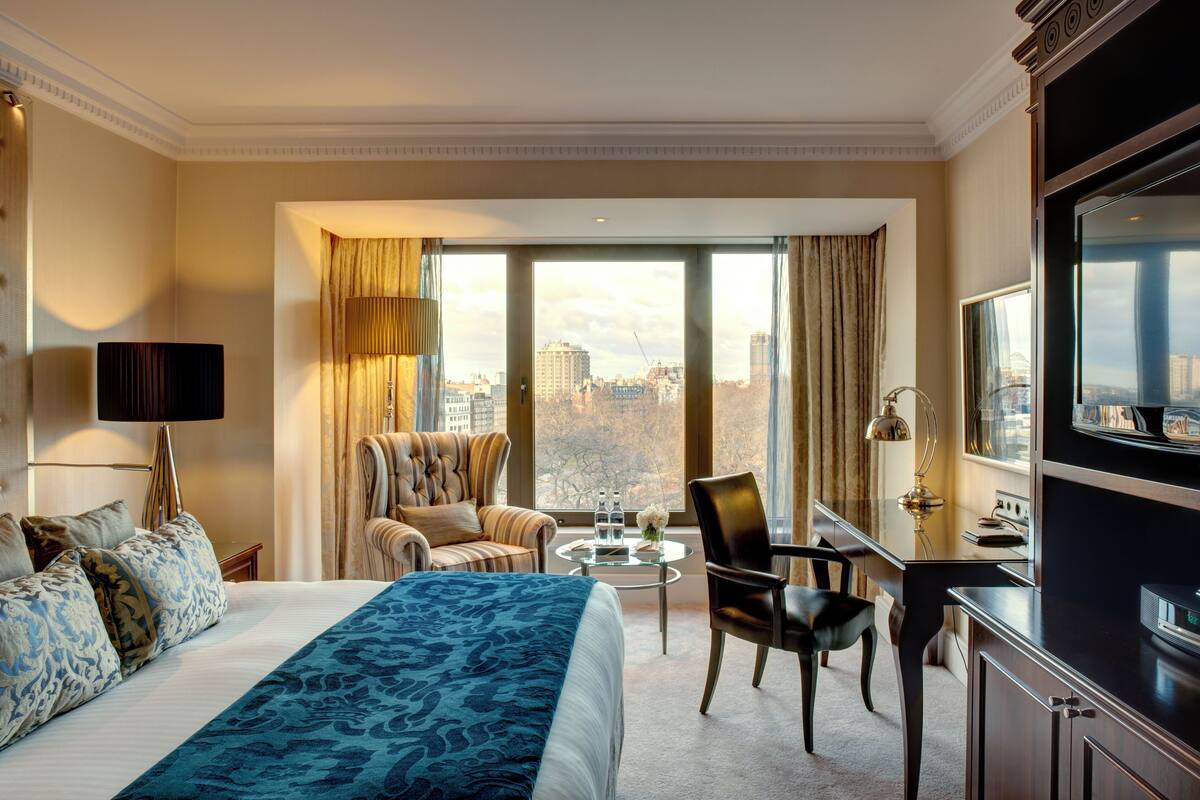 A hotel room with a large bed, a desk, two chairs, a TV, and a view of the city.