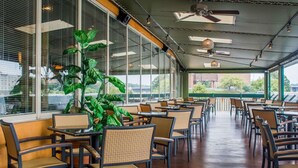 An indoor dining area with tables and chairs, large windows, ceiling fans, and a view of the outside. - Clarion Hotel & Suites Riverfront (Oswego)