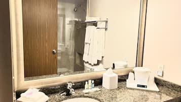 A bathroom with a large mirror, a sink, a towel rack, and a shower area.